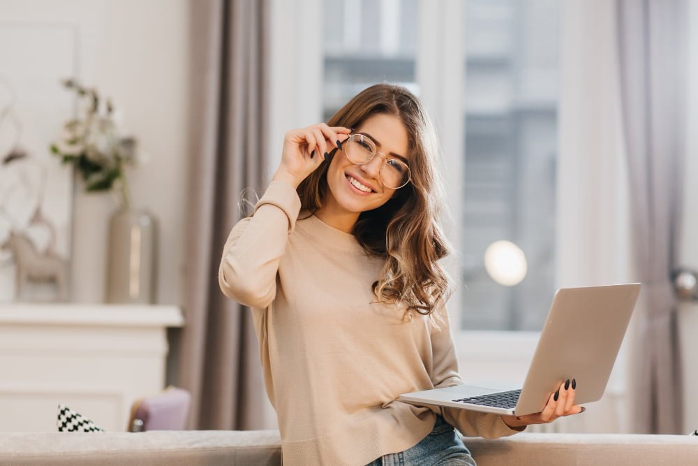 Qual a melhor internet do Brasil? Confira aqui 3 cute girl beige shirt touching glasses holding laptop with smile