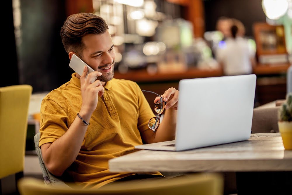 Qual a melhor internet do Brasil? Confira aqui 4 young happy freelancer working computer while talking smart phone bar