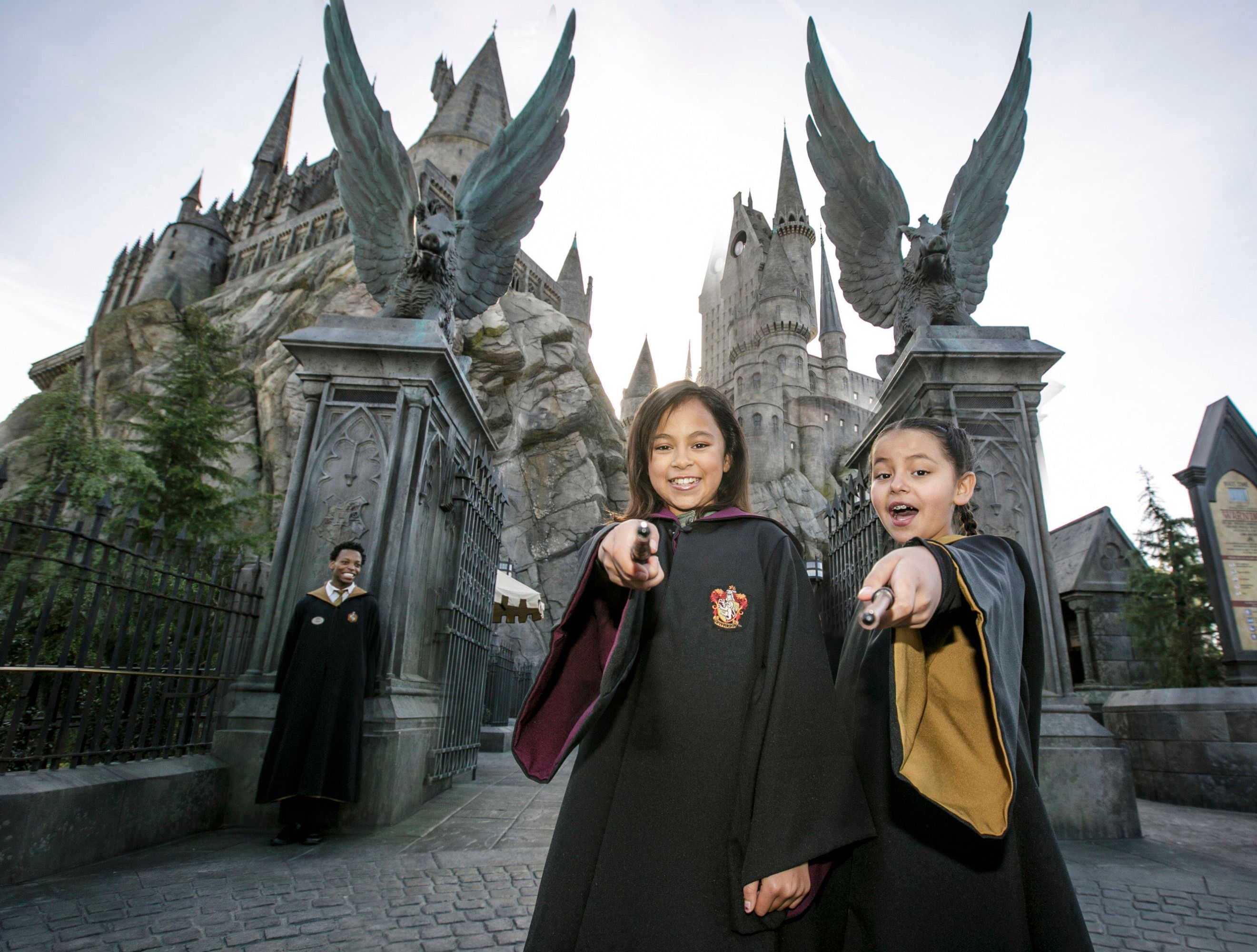 Duas garotas em trajes de Harry Potter agitando varinhas