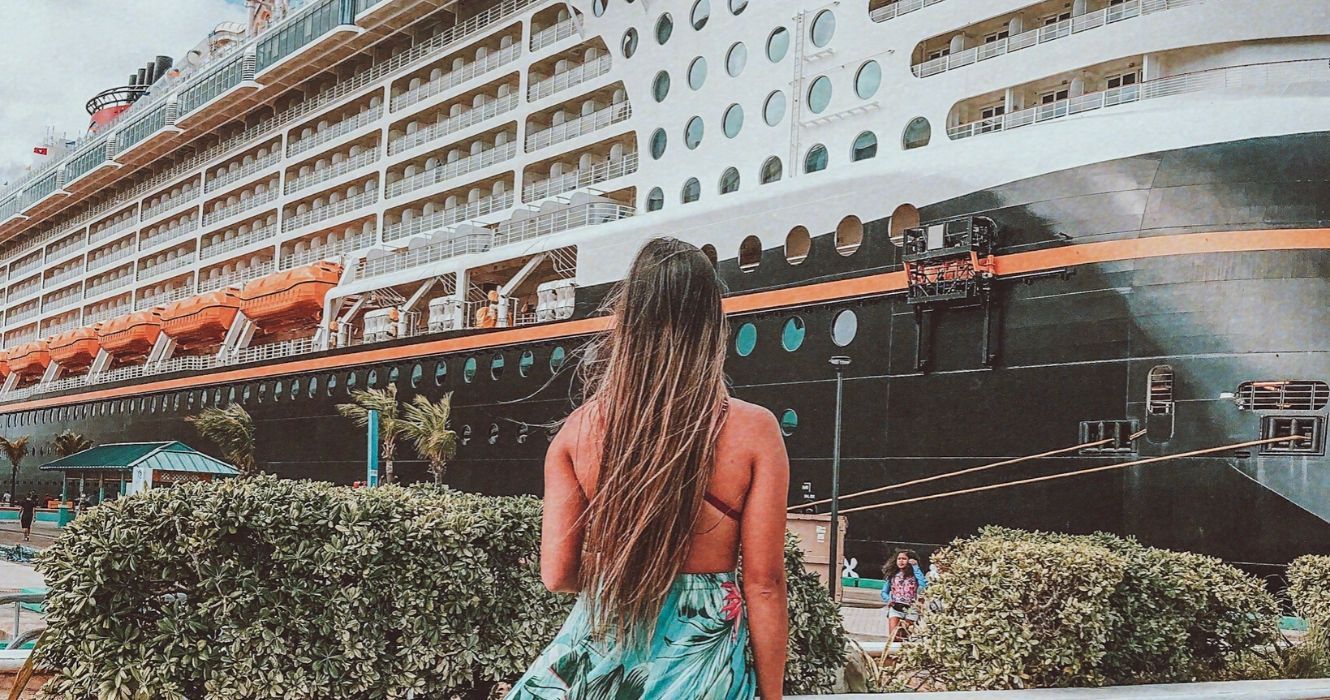 20 fatos que os agentes de viagens acham que os turistas devem considerar antes de reservar um cruzeiro 1 Mulher olhando para o navio de cruzeiro Disney no porto