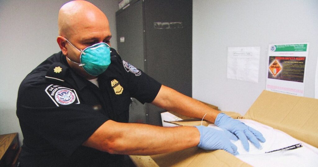 Border patrol agent wearing a mask and gloves opening a box