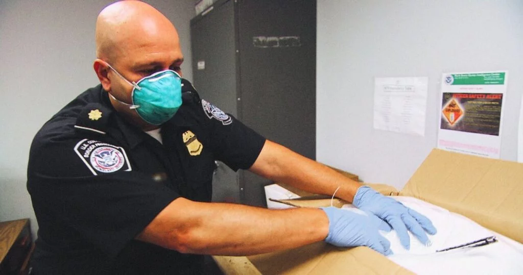 Histórias de 'segurança de fronteira' que a Netflix quer varrer para debaixo do tapete 9 Border patrol agent wearing a mask and gloves opening a box