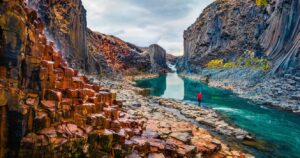 a person standing near a glacial river in iceland surrounded by basalt cliffs