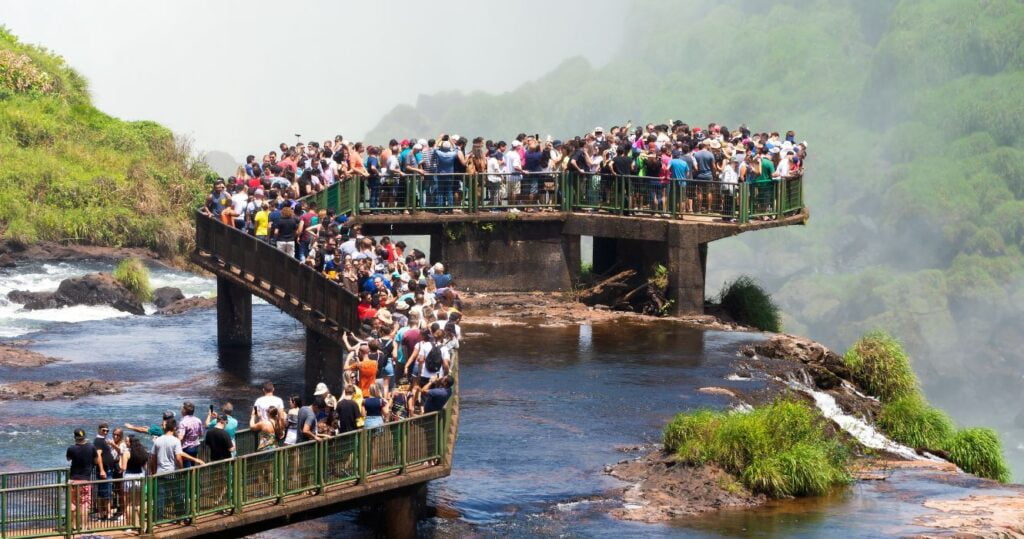 O que é excesso de turismo e o que podemos fazer para impedi-lo? 4 tourists crowded on iguasso bridge in brazil, overtourism