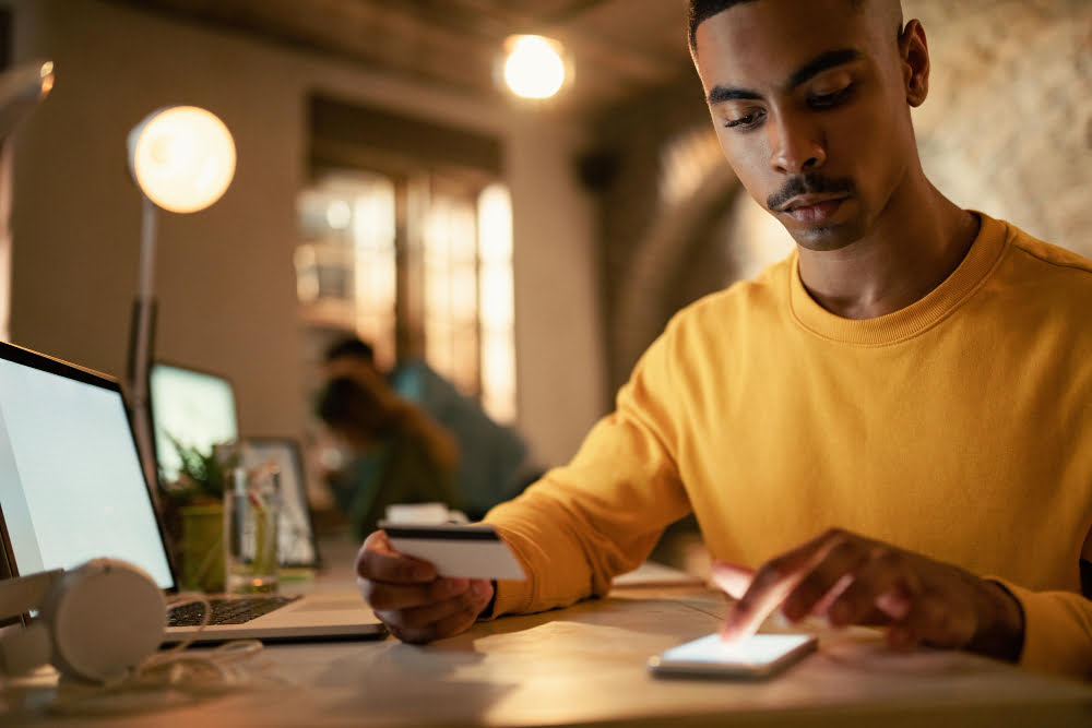 Banco Digital para quem tem o nome sujo 2 african american businessman using credit cart mobile phone while checking his online bank account during late night work office