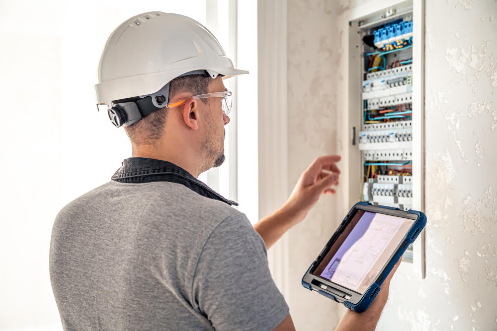 Qual o tamanho da caixa do medidor de energia elétrica? 4 man electrical technician working switchboard with fuses uses tablet 2