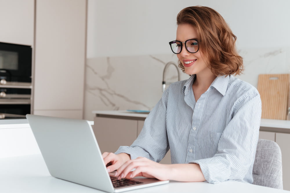 Trabalhar em Casa: Desafios e Estratégias para uma Rotina Produtiva 3 elegant smiling woman glasses striped shirt using laptop computer while siting table kitchen